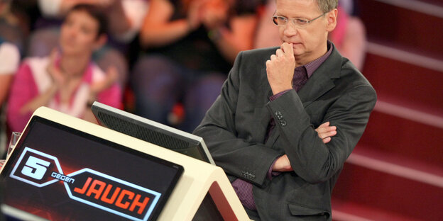 Herr Jauch grübelnd das Gesicht in die Hand gestützt, vor ihm ein Display, das seinen Namen anzeigt Herr Jauch grübelnd das Gesicht in die Hand gestützt, vor ihm ein Display, das seinen Namen anzeigt