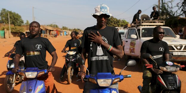 In der Bildmitte steht ein junger Mann mit Hut und Sonnenbrille. Die Hand liegt auf seiner Brust, er singt die Nationalhymne. Rechts und Links von ihm sitzen und stehen ebenfalls junge Männer. Sie alle tragen schwarze T-Shirts der Bürgerbewegung. In der Bildmitte steht ein junger Mann mit Hut und Sonnenbrille. Die Hand liegt auf seiner Brust, er singt die Nationalhymne. Rechts und Links von ihm sitzen und stehen ebenfalls junge Männer. Sie alle tragen schwarze T-Shirts der Bürgerbewegung.