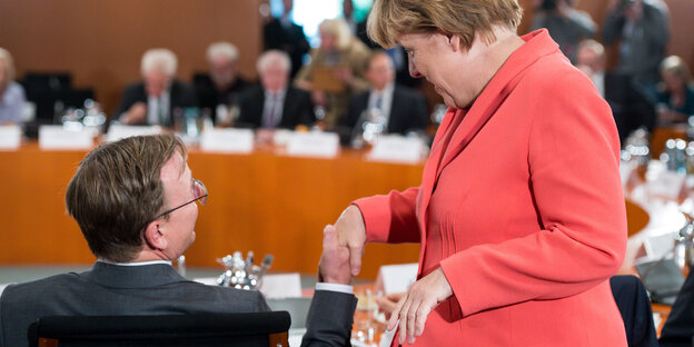 Ramelow, sitzend, und Merkel, sthehen, reichen sich die Hand Ramelow, sitzend, und Merkel, sthehen, reichen sich die Hand