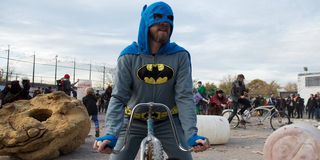 Ein Mann im Batman-Kostüm sitzt auf einem Fahrrad Ein Mann im Batman-Kostüm sitzt auf einem Fahrrad