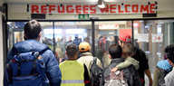 Flüchtlinge gehen am Flensburger Bahnhof unter einem Transparent "Refugees Welcome" hindurch.