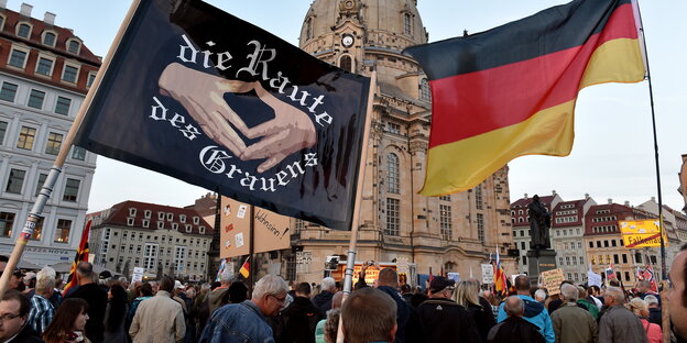 Pegida-Anhänger vor der Frauenkirche mit Deutschlandfahne und einem Transparent auf dem „die Raute des Grauens“ steht Pegida-Anhänger vor der Frauenkirche mit Deutschlandfahne und einem Transparent auf dem „die Raute des Grauens“ steht