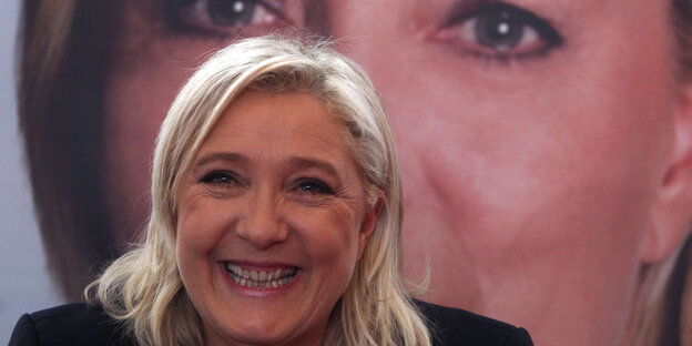 Marine Le Pen sitzt lächelnd vor einem großen Foto von ihr selbst Marine Le Pen sitzt lächelnd vor einem großen Foto von ihr selbst