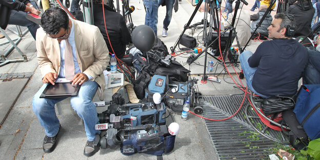 Ein Mann mit einem Tabletcomputer sitzt neben Fernsehkameras Ein Mann mit einem Tabletcomputer sitzt neben Fernsehkameras