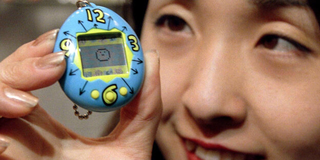Eine Frau hält ein Tamagotchi hoch Eine Frau hält ein Tamagotchi hoch