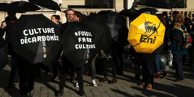 Klimaaktivist_innen halten schwarze Regenschirme mit Parlen gegen die Nutzung fossiler Brennstoffe hoch Klimaaktivist_innen halten schwarze Regenschirme mit Parlen gegen die Nutzung fossiler Brennstoffe hoch