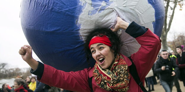 Eine Frau trägt einen Globus und reckt die Faust in die Höhe. Eine Frau trägt einen Globus und reckt die Faust in die Höhe.