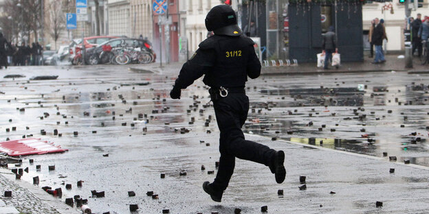 Ein Polizist in voller Kampfmonitur auf einer von Pflastersteinen übersäten Straße Ein Polizist in voller Kampfmonitur auf einer von Pflastersteinen übersäten Straße