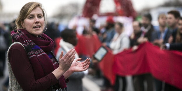 Eine Frau klatscht in die Hände, im Hintergrund stehen DemonstrantInnen Eine Frau klatscht in die Hände, im Hintergrund stehen DemonstrantInnen