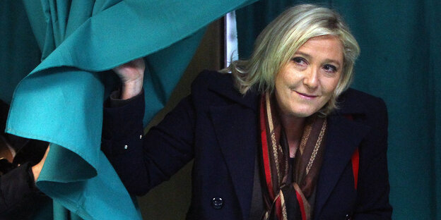 Marine Le Pen schaut hinter dem Vorhang einer Wahlkabine hervor. Marine Le Pen schaut hinter dem Vorhang einer Wahlkabine hervor.