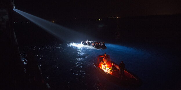 Von Scheinwerfern angestrahltes, voll besetztes Boot im Wasser bei Nacht. Von Scheinwerfern angestrahltes, voll besetztes Boot im Wasser bei Nacht.