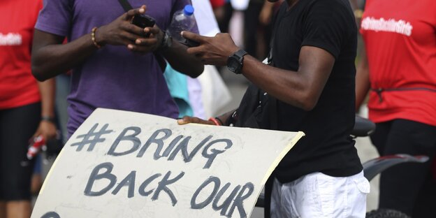 Zwei Nigerianer an ihren Mobilfunkgeräten über einem Kampagnenschild Zwei Nigerianer an ihren Mobilfunkgeräten über einem Kampagnenschild