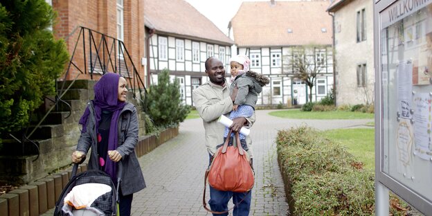 Eine Frau schiebt einen leeren Kinderwagen, ein Mann hat ein Kind auf dem Arme, im Hintergrund Fachwerkhäuser Eine Frau schiebt einen leeren Kinderwagen, ein Mann hat ein Kind auf dem Arme, im Hintergrund Fachwerkhäuser