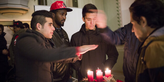 Vier Flüchtlinge in einer Kirche, sie wärmen ihre Hände über den Kerzen auf einem Adventskranz Vier Flüchtlinge in einer Kirche, sie wärmen ihre Hände über den Kerzen auf einem Adventskranz
