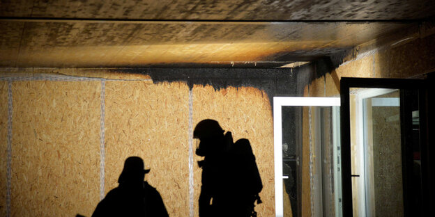 Der Schatten der Feuerwehrmänner an der Wand, vor einem geöffneten Fenster.