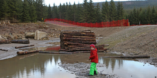 Kind in Riesenpfütze vor einem Holzstapel am Waldrand. Kind in Riesenpfütze vor einem Holzstapel am Waldrand.