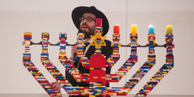 Ein Rabbi steht singend hinter einem Chanukka-Leuchter aus Legosteinen Ein Rabbi steht singend hinter einem Chanukka-Leuchter aus Legosteinen