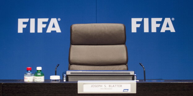 Ein leerer Stuhl vor einer blauen Wand mit der Aufschrift "Fifa" Ein leerer Stuhl vor einer blauen Wand mit der Aufschrift "Fifa"