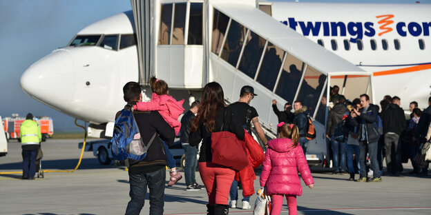 Menschen laufen auf einem Rollfeld auf ein Flugzeug zu Menschen laufen auf einem Rollfeld auf ein Flugzeug zu
