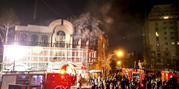 Nacht, erleuchtetes Gebäude, aus dessen Fenster Rauch steigt, davor Menschen und ein Feuerwehrauto Nacht, erleuchtetes Gebäude, aus dessen Fenster Rauch steigt, davor Menschen und ein Feuerwehrauto