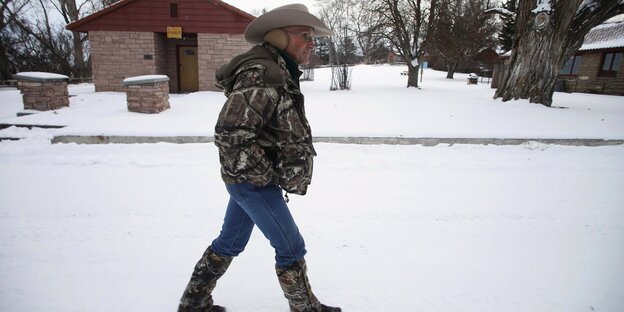 Ein Mann mit Cowboyhut und Cowboystiefeln läuft durch den Schnee Ein Mann mit Cowboyhut und Cowboystiefeln läuft durch den Schnee
