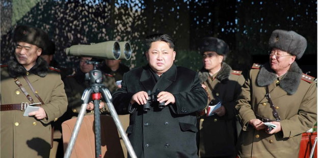 Kim Jong-un steht neben Männern in Uniform und einem Fernglas