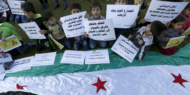 Kinder mit Plakaten über einer syrischen Flagge Kinder mit Plakaten über einer syrischen Flagge