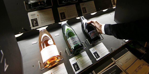 Eine Person zeigt auf eine Champagner-Flasche im Regal eines Weinladens. Eine Person zeigt auf eine Champagner-Flasche im Regal eines Weinladens.