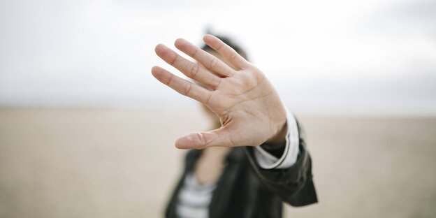 Eine Frau verbirgt ihr Gesicht hinter einer ausgestreckten Hand