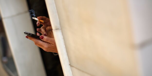 Rot lackierte Hände halten ein Smartphone und eine Zigarette Rot lackierte Hände halten ein Smartphone und eine Zigarette