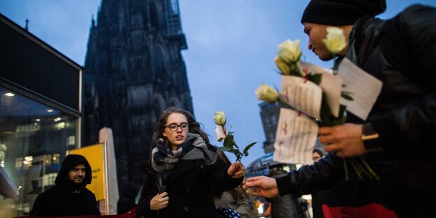 Ein Tunesier gibt einer Frau eine weiße Rose, dahinter der Kölner Dom Ein Tunesier gibt einer Frau eine weiße Rose, dahinter der Kölner Dom