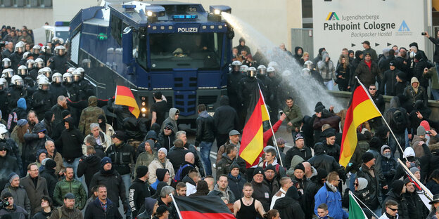 Eine Menschenmenge, im Hintergrund ein Wasserwerfer der Polizei, der im Einsatz ist Eine Menschenmenge, im Hintergrund ein Wasserwerfer der Polizei, der im Einsatz ist