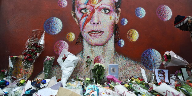 Blumen und Karten liegen vor einem Kunstwerk, das David Bowie zeigt Blumen und Karten liegen vor einem Kunstwerk, das David Bowie zeigt