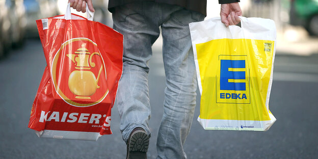Ein Mann trägt Plastiktüten von Kaisers und Edeka. Ein Mann trägt Plastiktüten von Kaisers und Edeka.