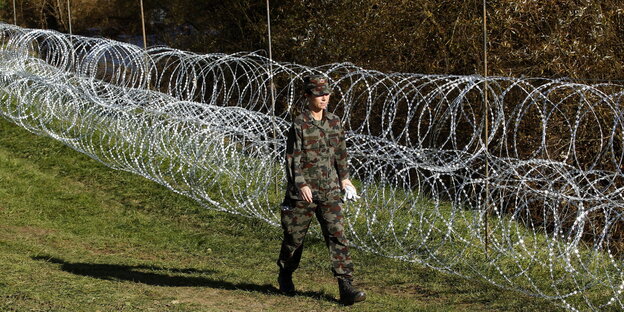 Soldat läuft an Zaun aus Stacheldrahtrollen entlang Soldat läuft an Zaun aus Stacheldrahtrollen entlang