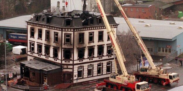 Ausgebranntes Haus vor dem zwei mobile Kräne stehen Ausgebranntes Haus vor dem zwei mobile Kräne stehen
