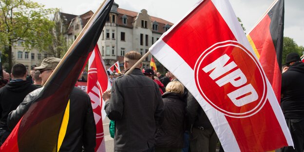 Menschen stehen mit Fahnen auf einem Platz. Auf einer steht „NPD“