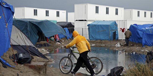Ein Migrant schiebt ein Fahrrad an der Großpfütze des Camps vorbei Ein Migrant schiebt ein Fahrrad an der Großpfütze des Camps vorbei