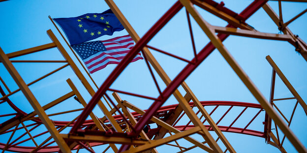 Achterbahnschiene, darüber wehen die Flaggen der EU und der USA Achterbahnschiene, darüber wehen die Flaggen der EU und der USA