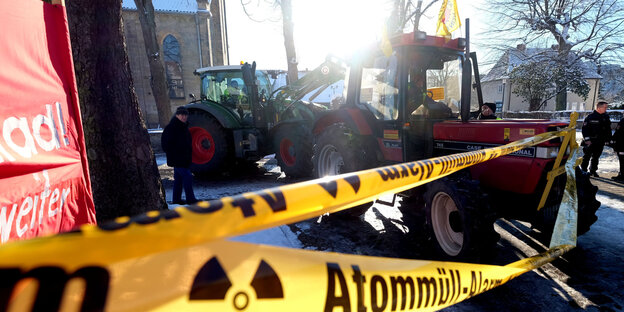 Ein schwarz-gelbes Absperrband mit „Atommüll“-Aufschrift, dahinter stehen Traktoren Ein schwarz-gelbes Absperrband mit „Atommüll“-Aufschrift, dahinter stehen Traktoren