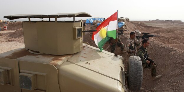 Ein Panzer mit einer kurdischen Flagge, davor in einem Schützengraben Soldaten Ein Panzer mit einer kurdischen Flagge, davor in einem Schützengraben Soldaten
