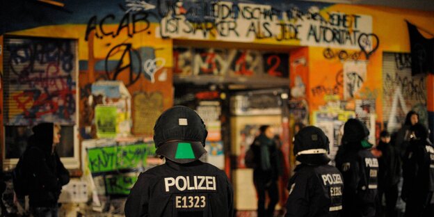 Polizisten in schwarzer Montur stehen mit dem Rücken zur Kamera vor einem bunt bemalten Haus Polizisten in schwarzer Montur stehen mit dem Rücken zur Kamera vor einem bunt bemalten Haus