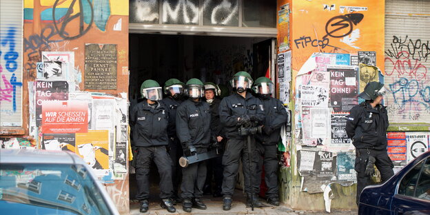 Polizisten stehen dicht gedrängt in der Toreinfahrt eines buntbemalten und mit Plakaten beklebten Hauses Polizisten stehen dicht gedrängt in der Toreinfahrt eines buntbemalten und mit Plakaten beklebten Hauses