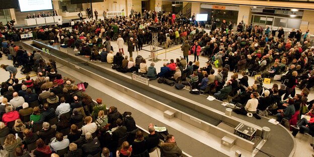 Menschen stehen um ein Fließband in einer Halle Menschen stehen um ein Fließband in einer Halle