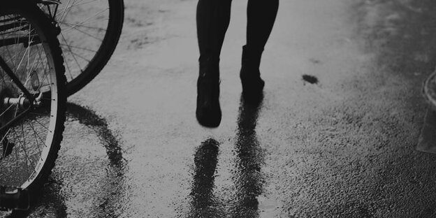 Ausschnitt des Schwarz-weiß-Bildes, der Füße und Waden einer Frau zeigt, die an Fahrradreifen vorbeiläuft Ausschnitt des Schwarz-weiß-Bildes, der Füße und Waden einer Frau zeigt, die an Fahrradreifen vorbeiläuft