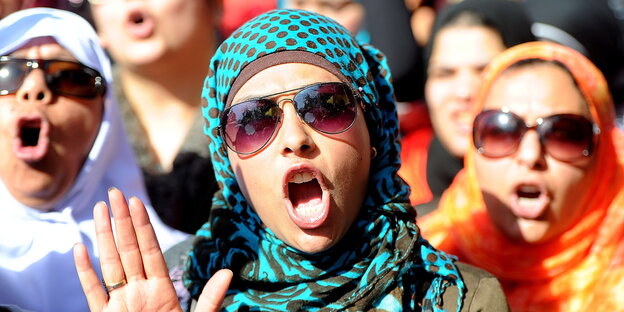 Drei ägyptische Frauen mit bunten Kopftüchern und Sonnenbrillen rufen Sprüche in einer Menge auf dem Tahrir-Platz. Drei ägyptische Frauen mit bunten Kopftüchern und Sonnenbrillen rufen Sprüche in einer Menge auf dem Tahrir-Platz.