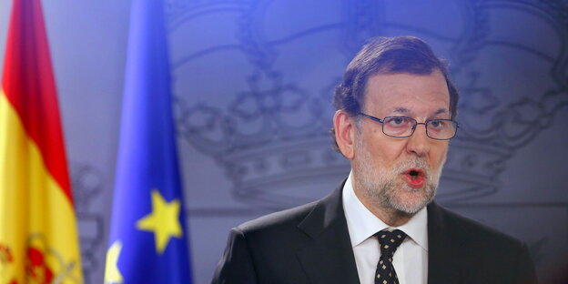 Rajoy mit offenem Mund neben einer spanischen und einer EU-Flagge