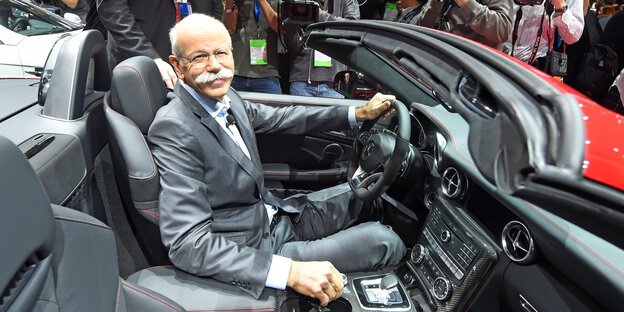 Der Daimler-Chef Dieter Zetsche sitzt am Steuer eines grau-roten Autos und lächelt Der Daimler-Chef Dieter Zetsche sitzt am Steuer eines grau-roten Autos und lächelt