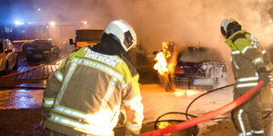 zwei Feuerwehrmänner löschen mit Schaum ein brennendes Auto
