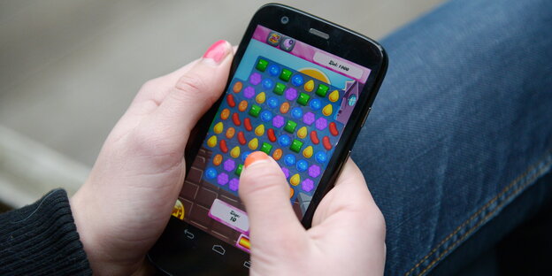 Eine Hand hält ein Smartphone. Auf dem Display ist ein Spiel zu sehen. Eine Hand hält ein Smartphone. Auf dem Display ist ein Spiel zu sehen.